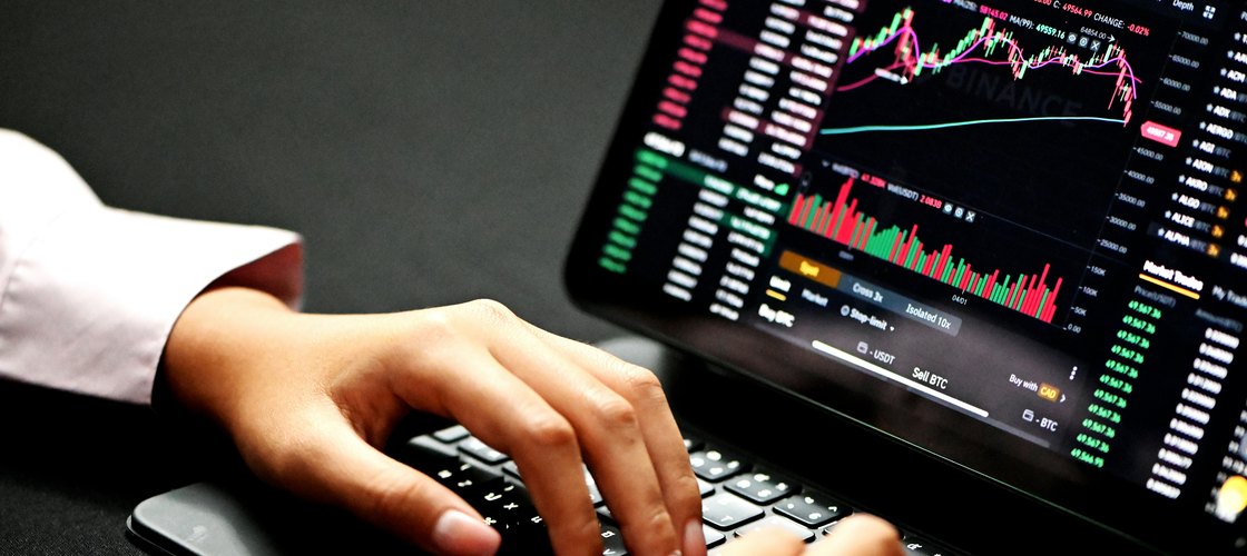 A trader at a laptop showing a live candlestick chart and order book