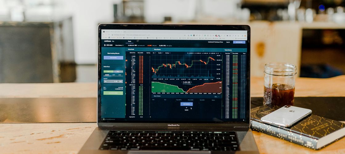 A laptop showing a live trading chart on a cafe table